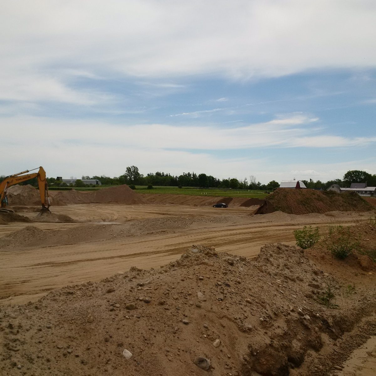 Excavator stripping topsoil at a pit